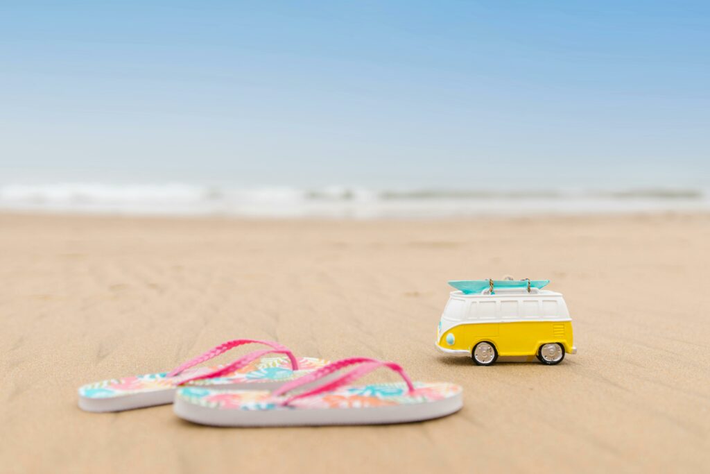 pexels-photo-8455963-8455963 Vibrant flip flops and a playful toy van on a sandy beach, perfect for vacation vibes.